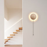 Travertine wall sconce with a pull-cord beside a floating timber staircase