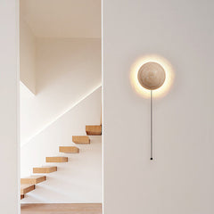 Travertine wall sconce with a pull-cord beside a floating timber staircase