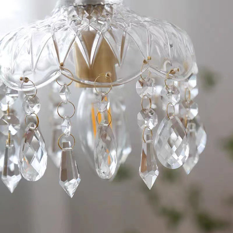 Close-up of a clear glass shade rim and crystal droplets over greenery