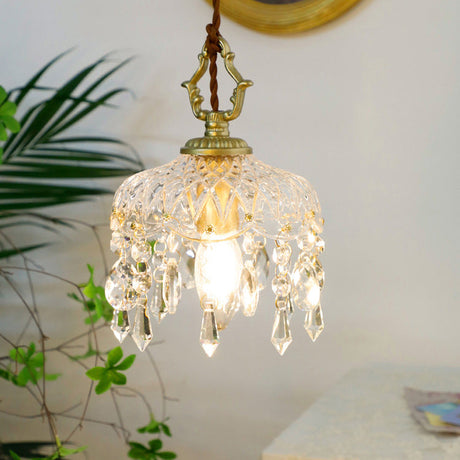 Crystal pendant light with a gold cap above a table beside a palm plant