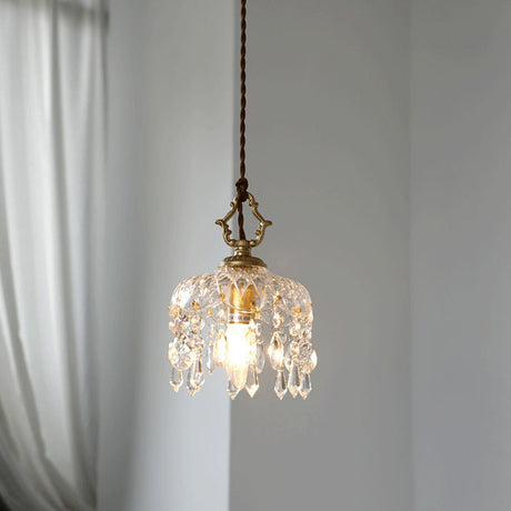 Lit crystal pendant light with a clear glass shade on a grey wall