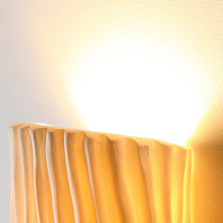 Top edge of a creamy yellow wall sconce with light glowing upward