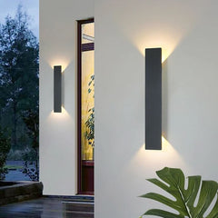 Two black up and down LED wall sconces beside a doorway on a light facade
