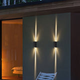 Two black up and down wall lights beside a glass wall and bedroom at dusk
