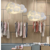 Two white cloud pendant lights over garment racks in a clothing boutique