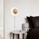 Stone LED sconce with a pull-chain above a marble bedside table in a bedroom