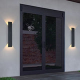 Black exterior wall light on a stone facade near a garden bed