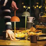 Hand carrying an orange cordless lamp to an outdoor evening table with string lights