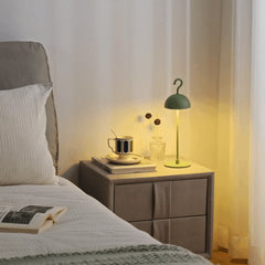 Green rechargeable dome lamp glowing on a bedside cabinet next to a made bed