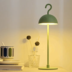 Green portable table lamp lit on a desk beside a coffee cup and dried flowers