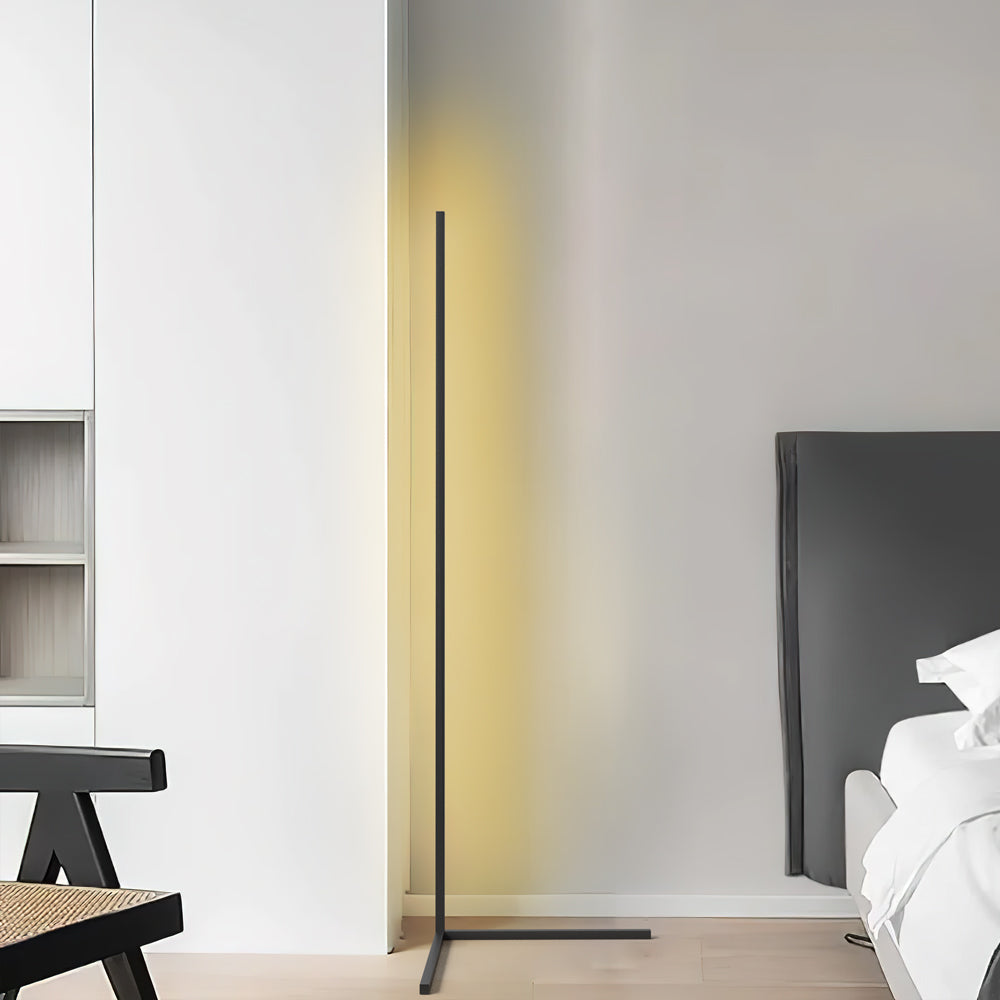 Black corner floor lamp lighting a bedroom wall beside a grey headboard and bed