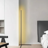 Black corner floor lamp lighting a bedroom wall beside a grey headboard and bed