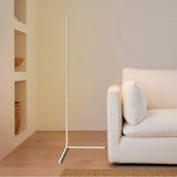 White corner floor lamp standing against a warm wall beside a cream sofa