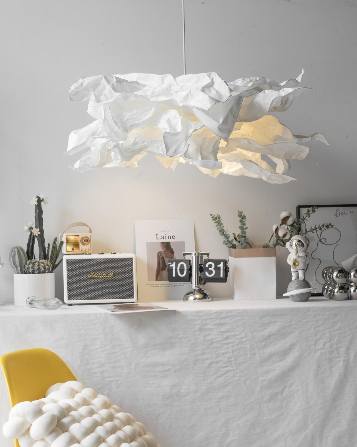 Paper pendant light above a shelf display with a yellow chair below