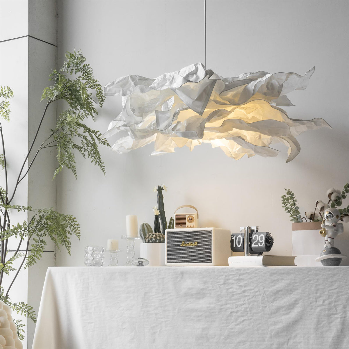 Paper pendant light above a linen covered table with candles and a fern