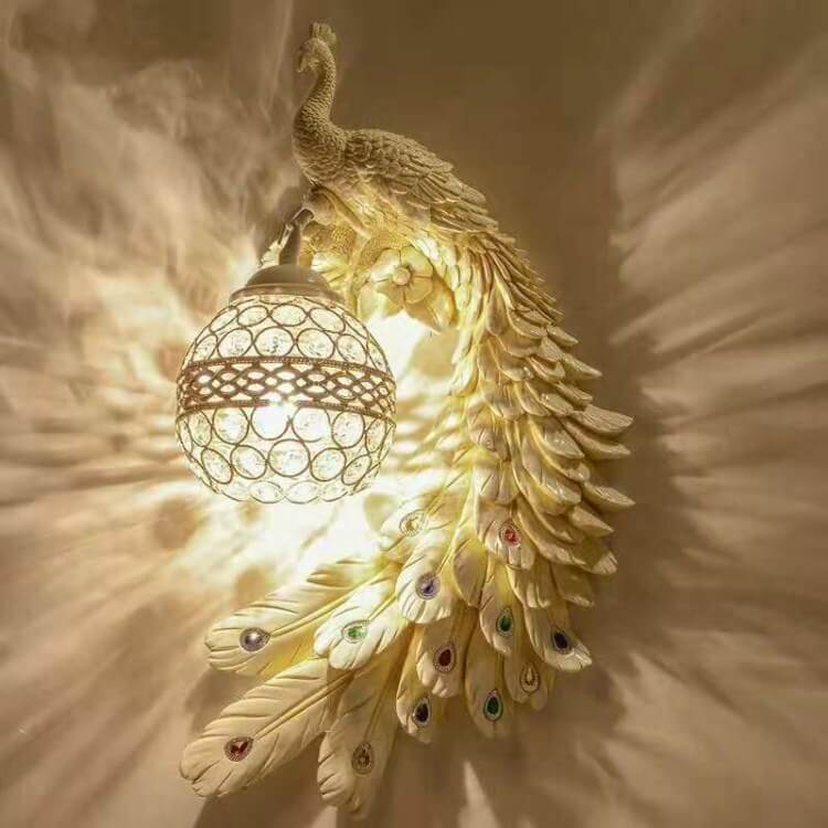 Ivory peacock wall sconce facing left casting warm feather-shaped shadows on the wall