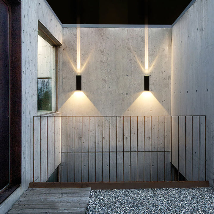 Two wall sconces on a concrete stairwell wall throwing up and down beams