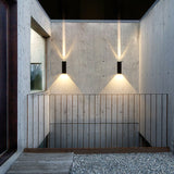 Two wall sconces on a concrete stairwell wall throwing up and down beams