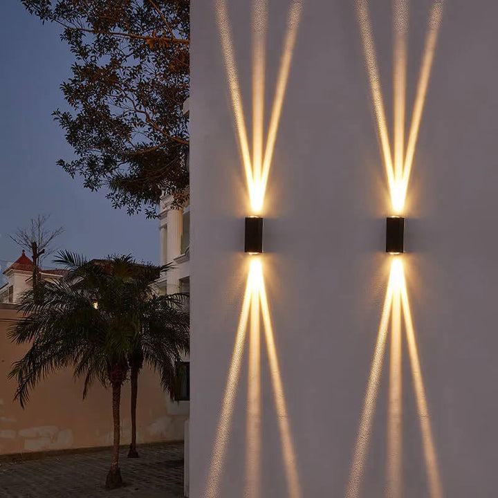 Wall sconces on a white wall by a palm tree casting sharp crossed beams