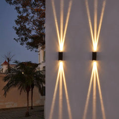 Wall sconces on a white wall by a palm tree casting sharp crossed beams