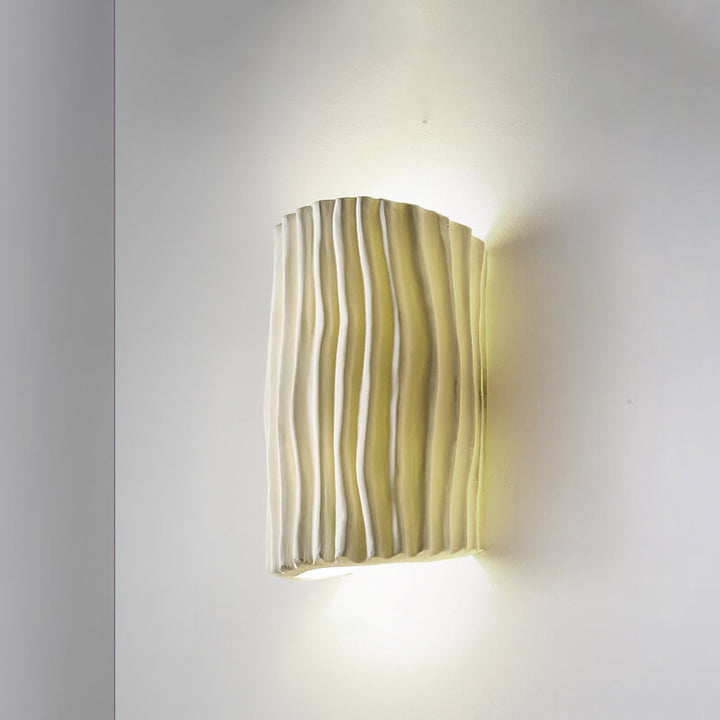 Creamy yellow half cylinder wall sconce lit on a plain wall