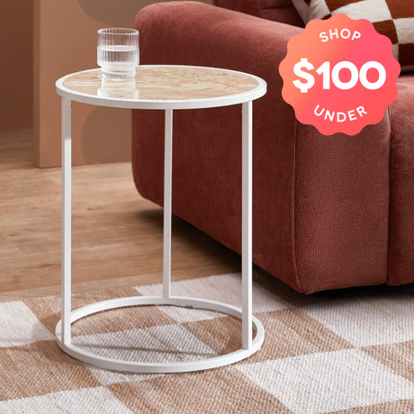 Small round white table with a glass of water next to a brown sofa, with a 'Shop $100 Under' label.