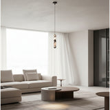 A modern living room featuring a minimalist beige sofa, a round wooden coffee table, and a distinctive pendant light with a textured, layered glass shade hanging from a thin black cord.