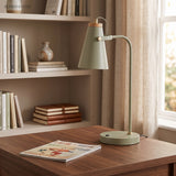 Green metal desk lamp on a walnut desk in front of book shelving