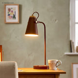 Rust brown desk lamp glowing warmly on a desk beside a mug