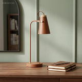 Rust toned metal desk lamp with cone shade on a walnut side table