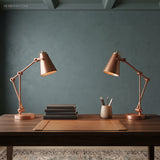 Two copper toned adjustable desk lamps on a dark wood writing table