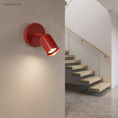Red spotlight wall sconce on a textured wall beside a staircase landing