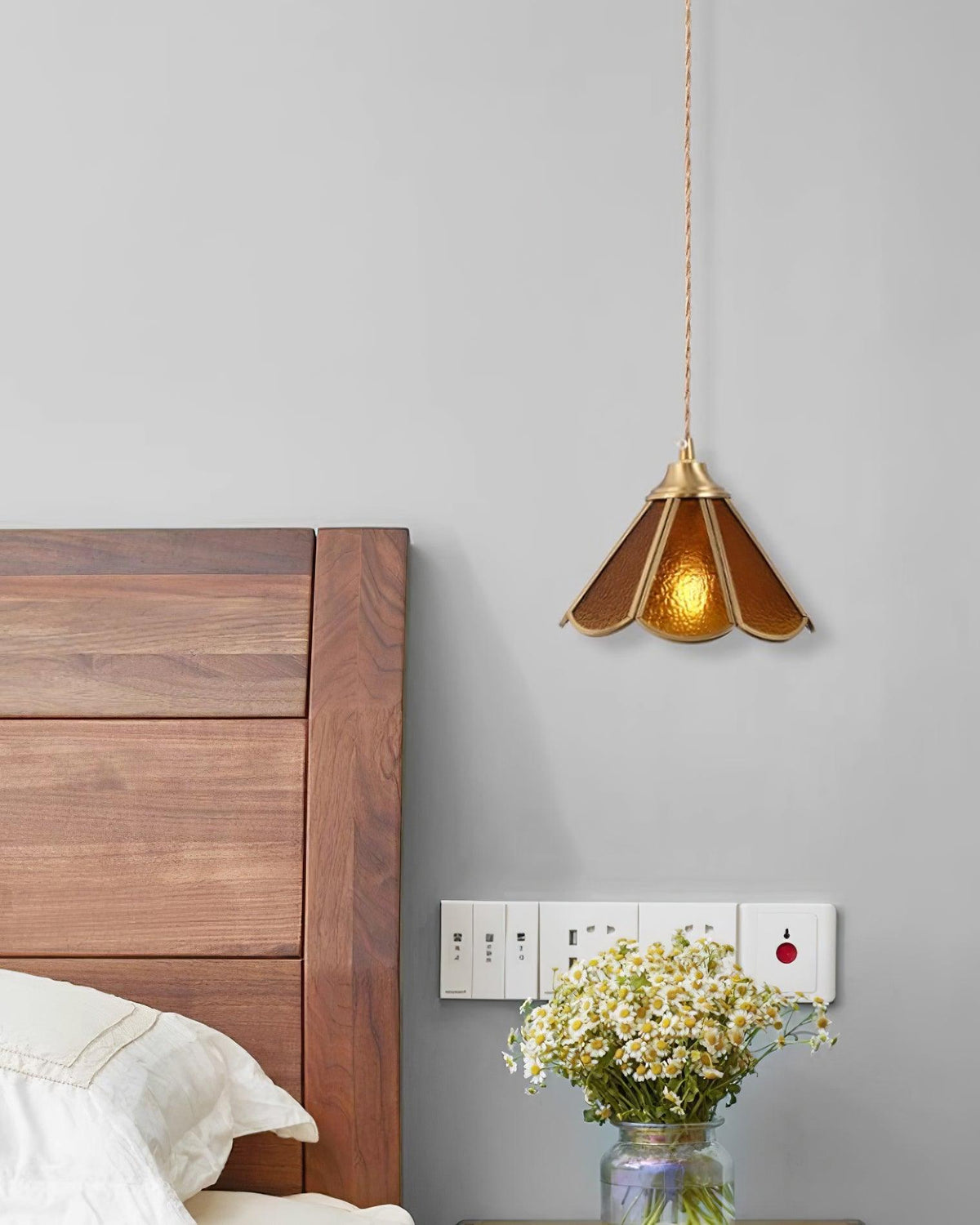Amber pendant lit above a bedside cabinet with a small vase of daisies