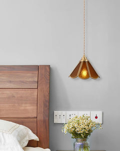 Amber pendant lit above a bedside cabinet with a small vase of daisies
