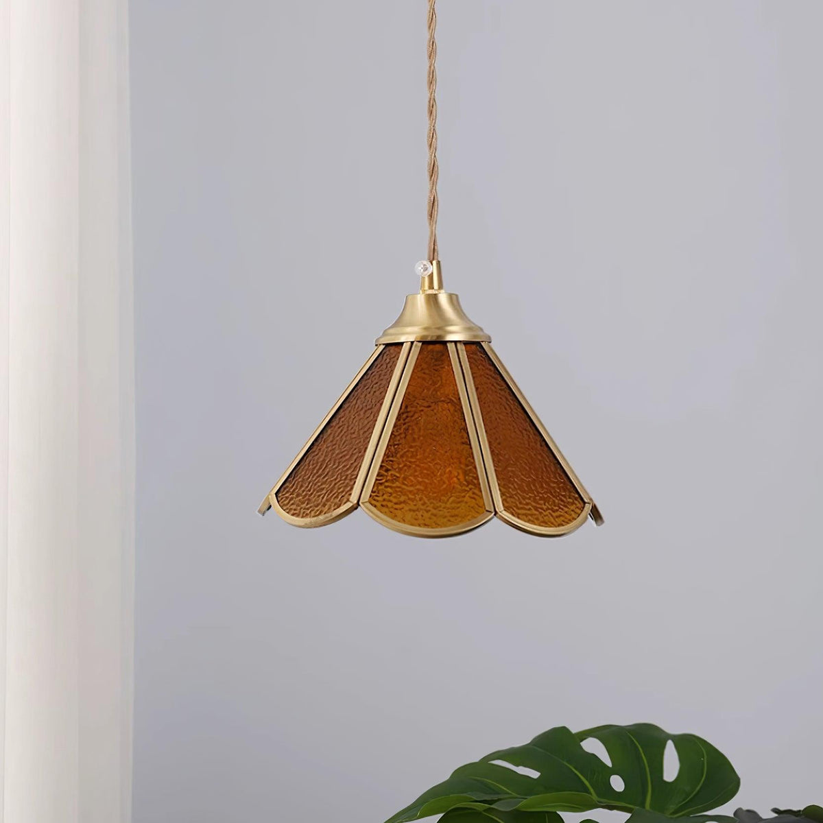 Amber glass pendant hanging beside a pale curtain with the panels unlit