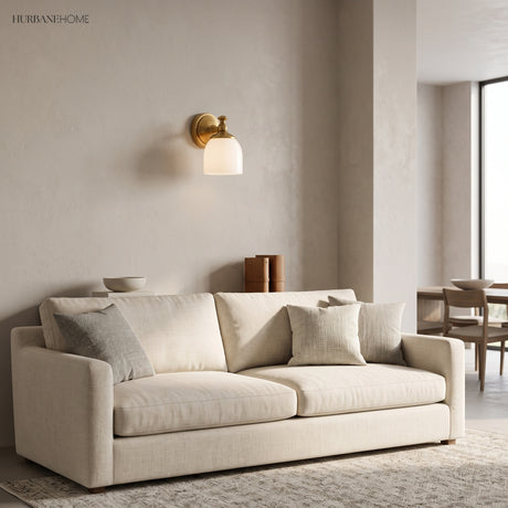 Single brass milk glass wall light above a pale sofa in a living room