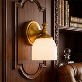 Antique brass sconce with milk glass bell shade on carved wood panelling