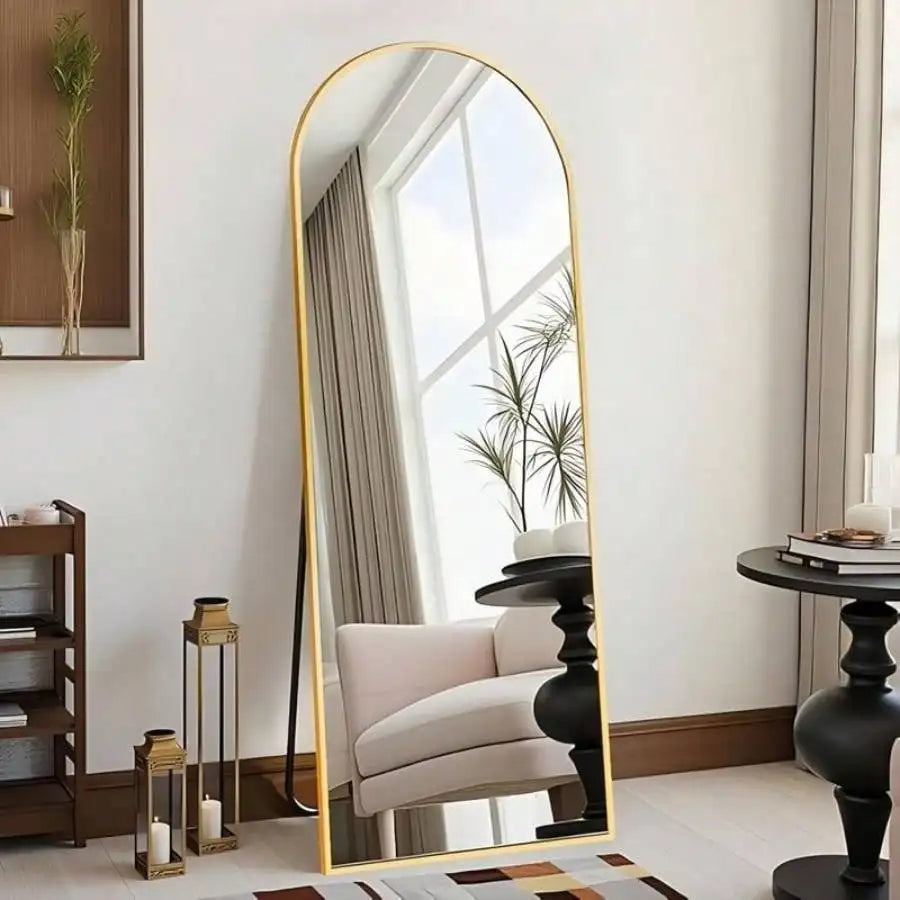 Arched gold full length mirror leaning against wall in bedroom