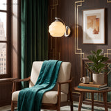 Glass globe wall sconce above a chair beside framed art and plant