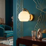 Art Deco opal glass globe wall sconce with gold arm on teal wall
