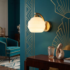 Art Deco opal glass globe wall sconce with gold arm on teal wall