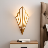 Gold fan sconce lit above a bedside table and upholstered headboard