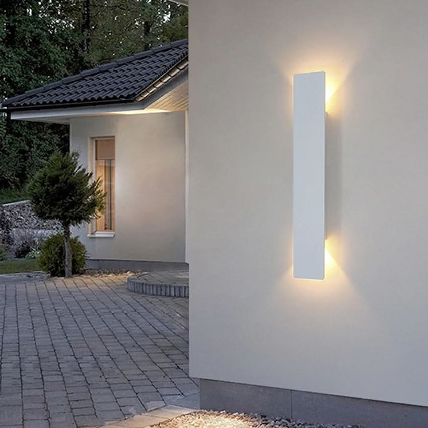 Long black LED wall sconce illuminating a modern outdoor courtyard
