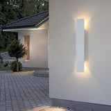 Long black LED wall sconce illuminating a modern outdoor courtyard