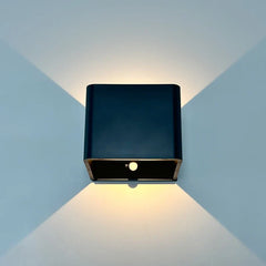 Black cube wall sconce lit on a blue wall showing both beams