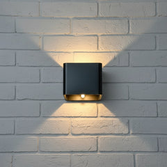 Black cube wall sconce lit on a white brick wall