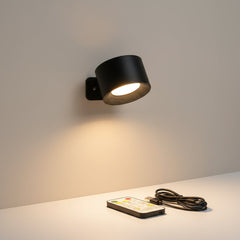 Black cordless sconce lit above a shelf beside a remote and cable