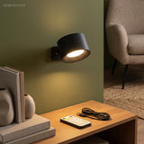 Black puck sconce lit on a green wall above a bookshelf