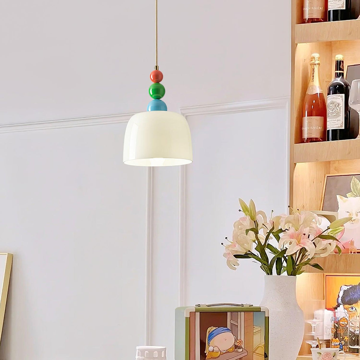 White shaded beaded pendant hanging in front of a shelf of bottles and flowers