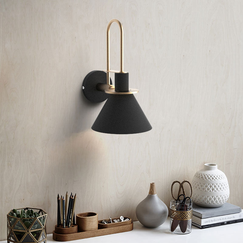 Black cone sconce above a desk holding pens, pots and books